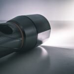 close up of a black camera lens lying on a white surface with soft light to the right