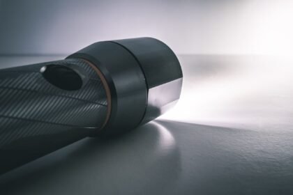 Close-up of a black camera lens lying on a white surface, with soft light to the right.
