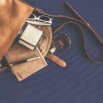 leather handbag flat lay with everyday carry essentials including sunglasses wallet and notebook