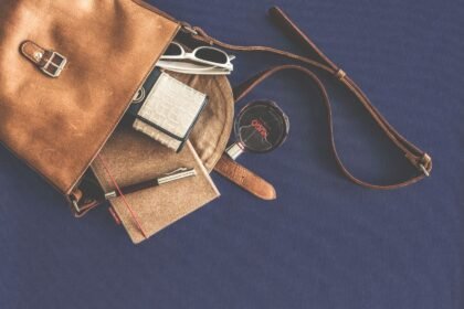 Leather handbag flat lay with everyday carry essentials including sunglasses, wallet and notebook