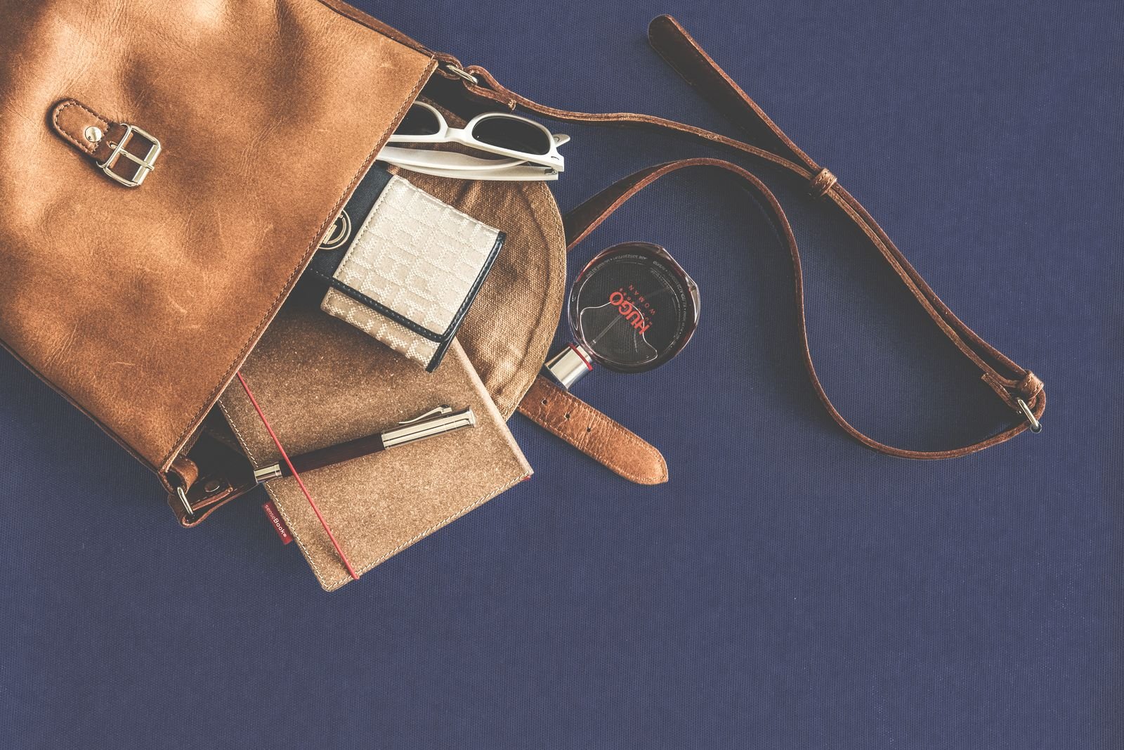 leather handbag flat lay with everyday carry essentials including sunglasses wallet and notebook