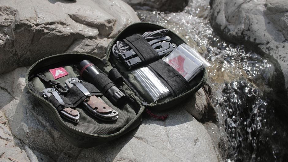 An outdoor survival kit laid out on rocks beside a stream