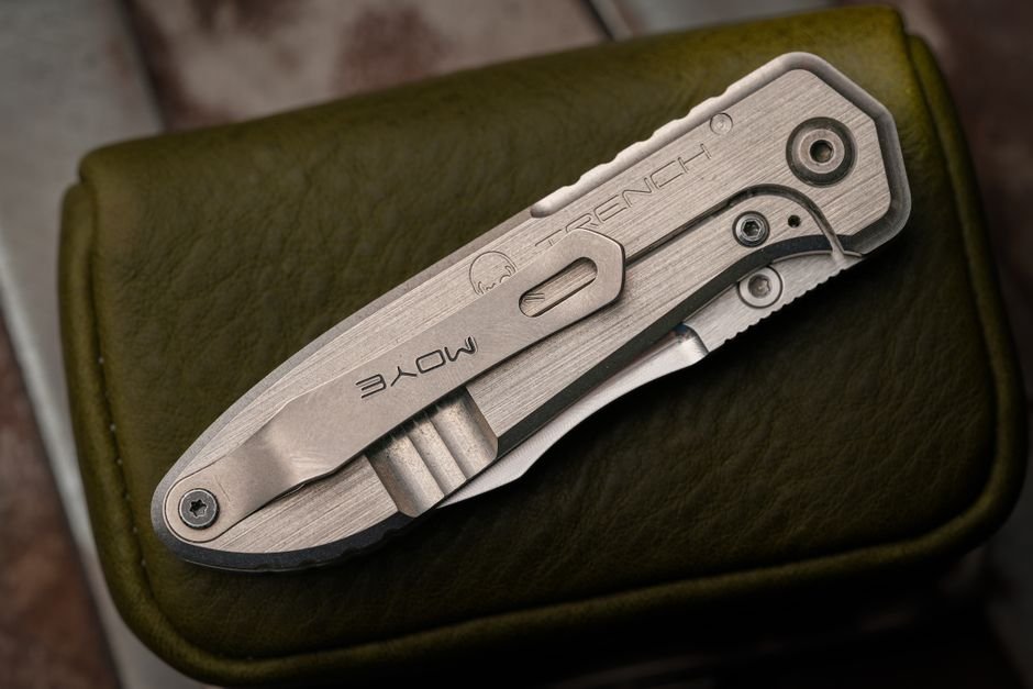 A folding knife resting on a textured leather surface