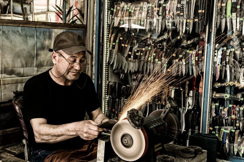 A craftsman sharpening knives in a workshop surrounded by tools