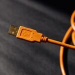close up of an orange usb a connector on a coiled orange cable against a dark blurred background