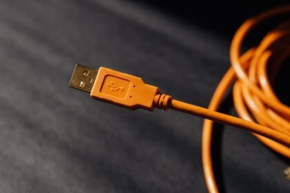 Close-up of an orange USB-A connector on a coiled orange cable against a dark blurred background.