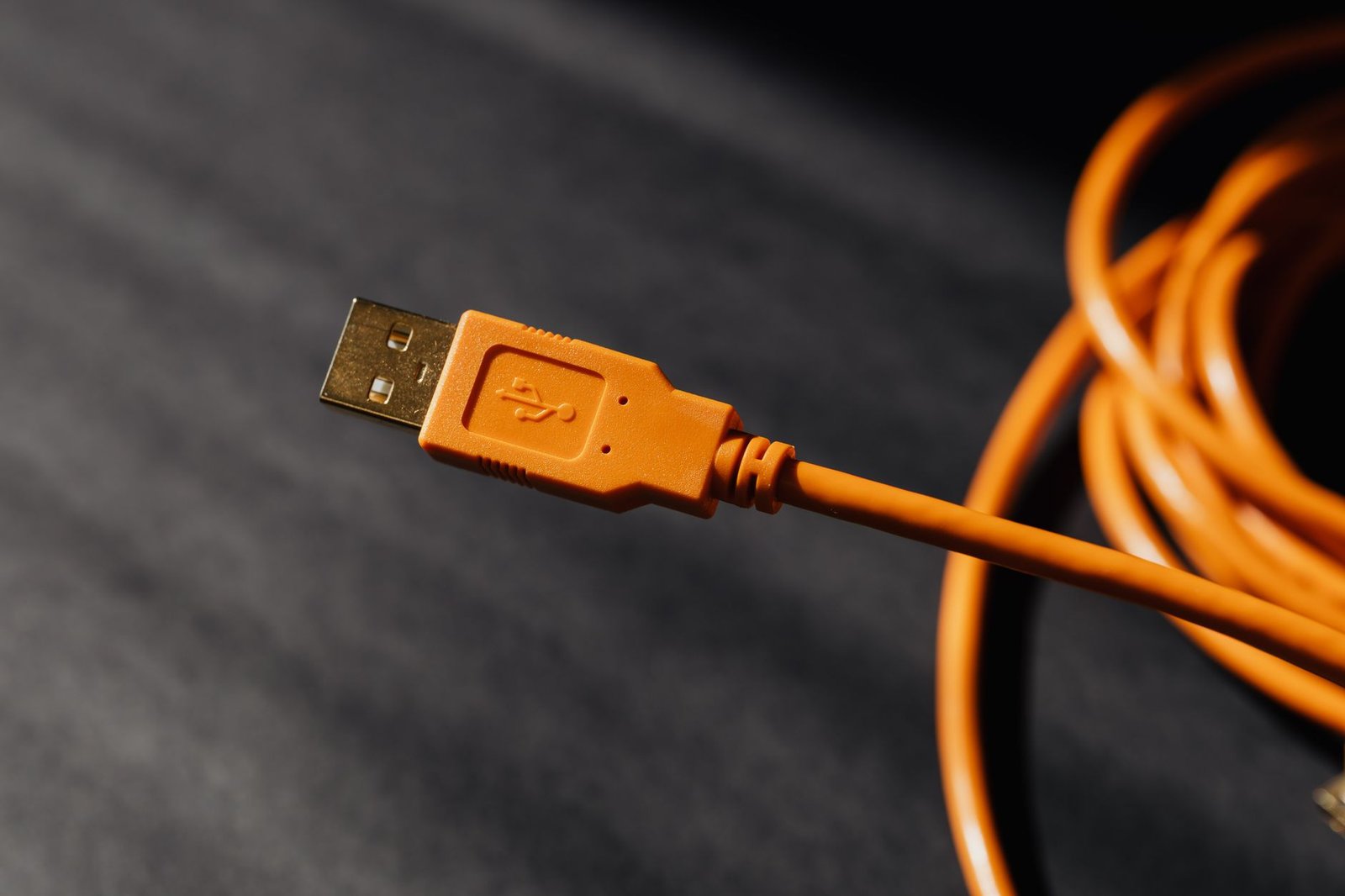close up of an orange usb a connector on a coiled orange cable against a dark blurred background