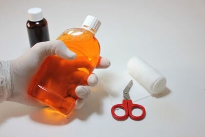 Hand holding an antiseptic bottle alongside first aid supplies for cleaning a wound