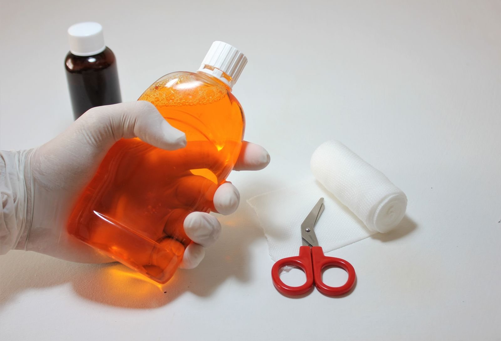 hand holding an antiseptic bottle alongside first aid supplies for cleaning a wound