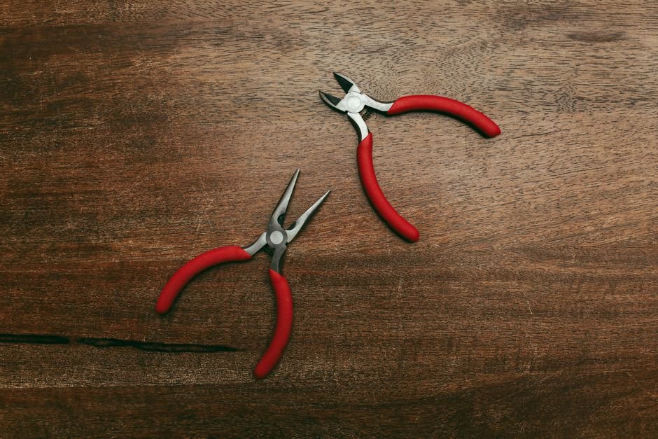 Two red-handled pliers resting on a wooden surface