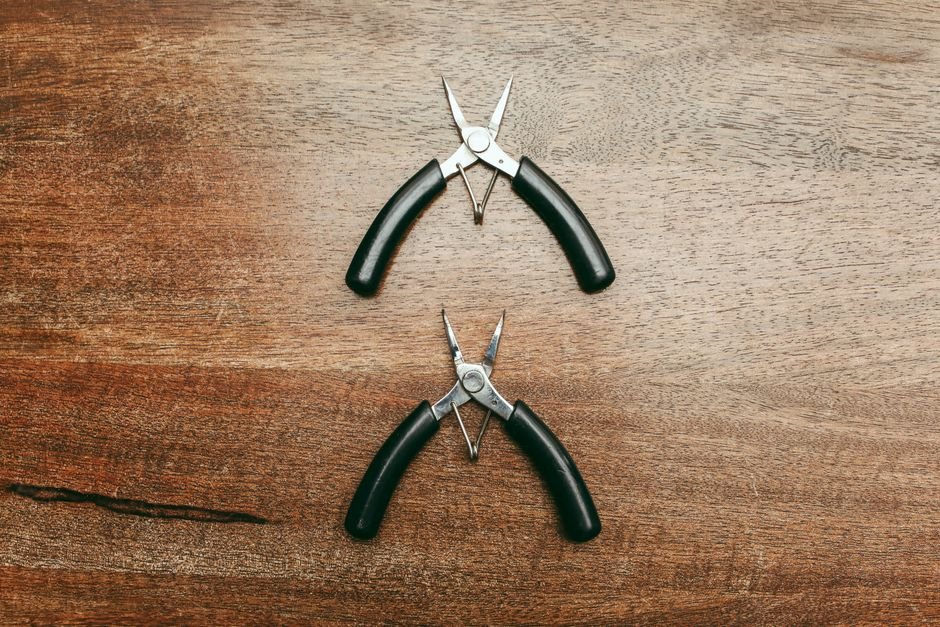 Two needle-nose pliers on a wooden tabletop