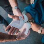 applying a bandage to an injured hand outdoors while assessing whether a cut needs stitches
