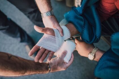 Applying a bandage to an injured hand outdoors while assessing whether a cut needs stitches