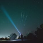 person shining a bright edc flashlight beam into a starry night sky