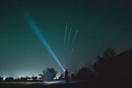 Person shining a bright EDC flashlight beam into a starry night sky