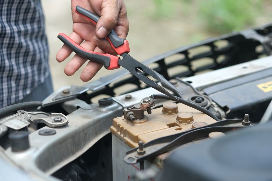 A person using pliers on a car battery outdoors