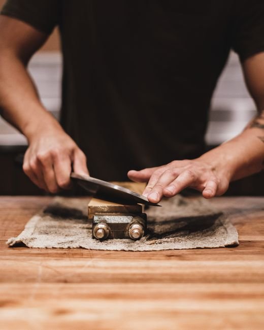 A person sharpening a knife on a whetstone, hands in focus