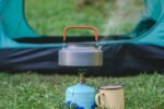 compact gas camping stove boiling a kettle beside a tent
