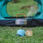 compact gas camping stove boiling a kettle beside a tent