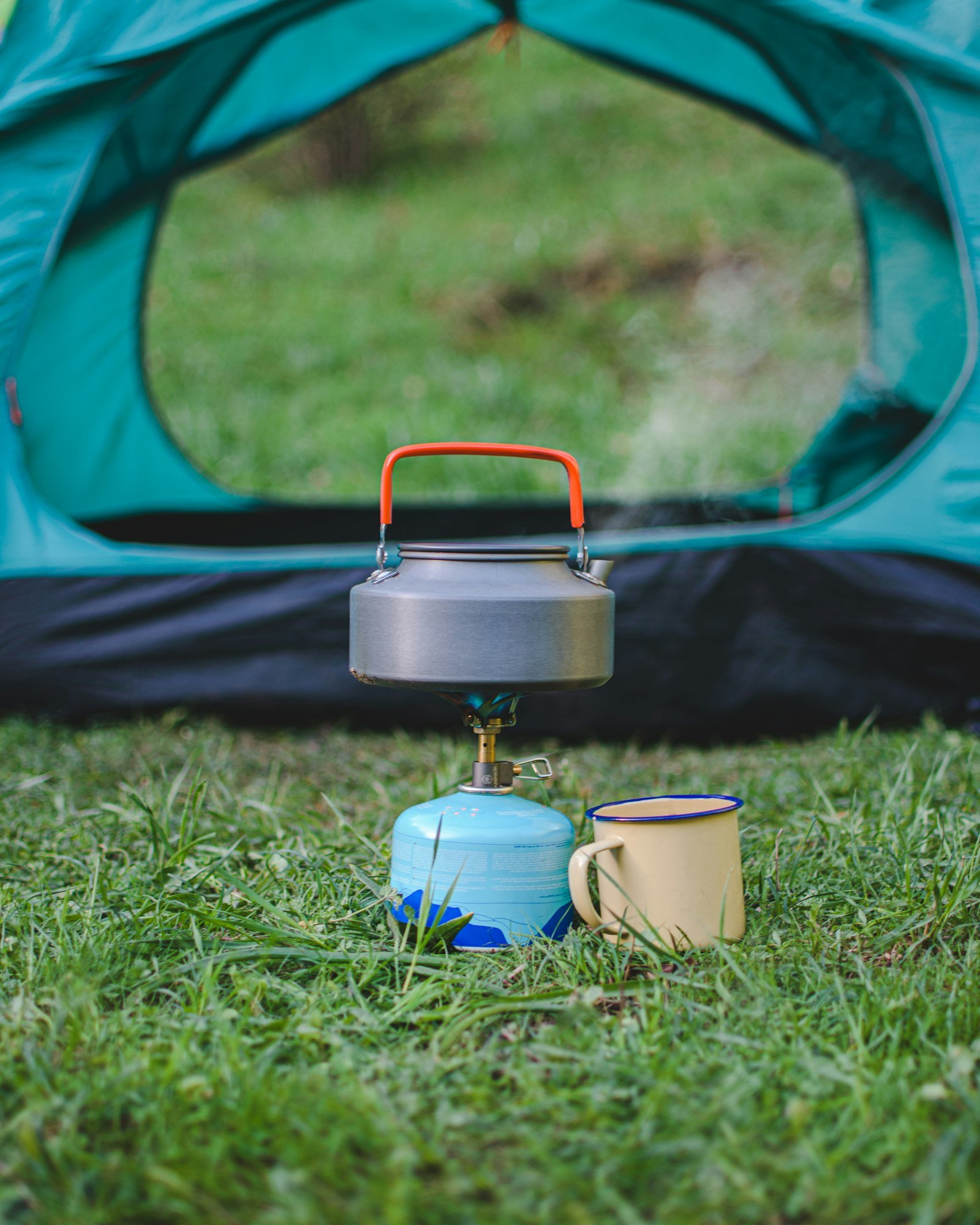 compact gas camping stove boiling a kettle beside a tent
