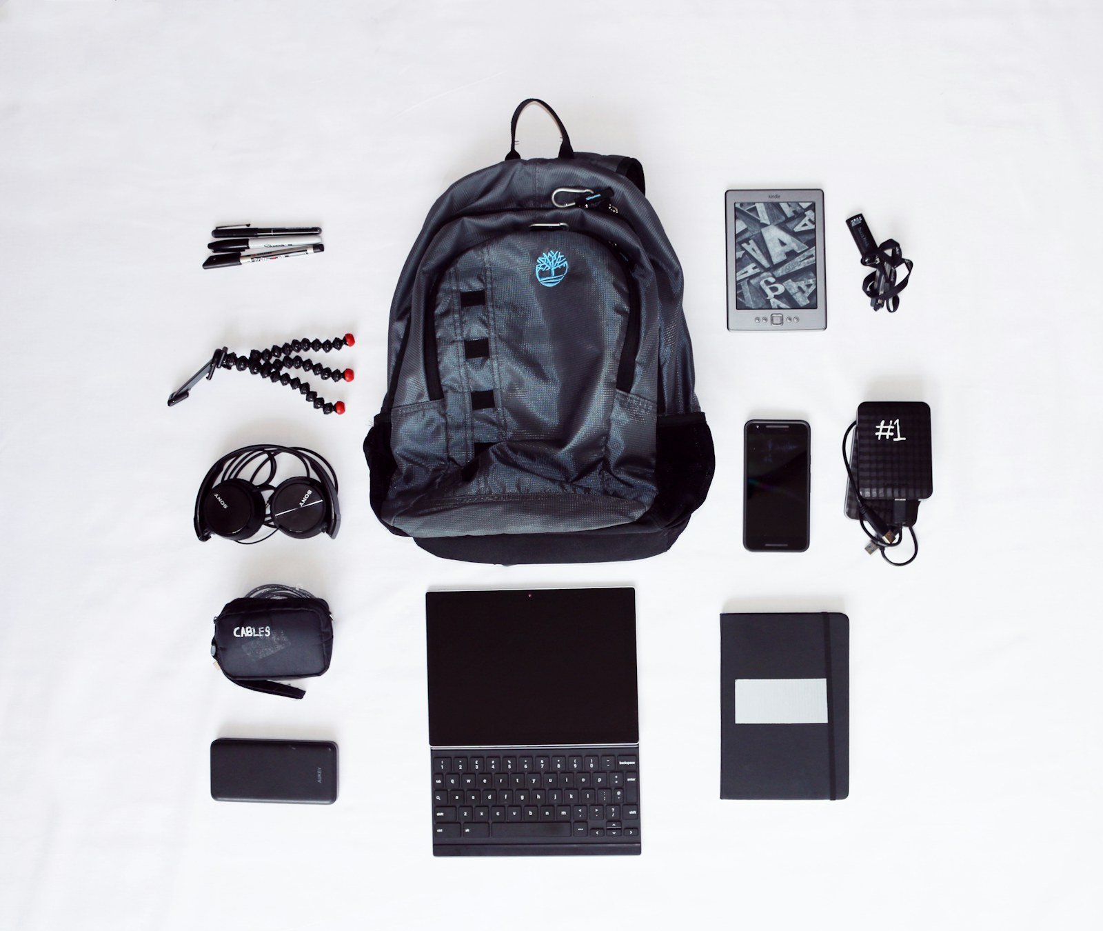 backpack laid out with laptop headphones smartphone and other commuter essentials