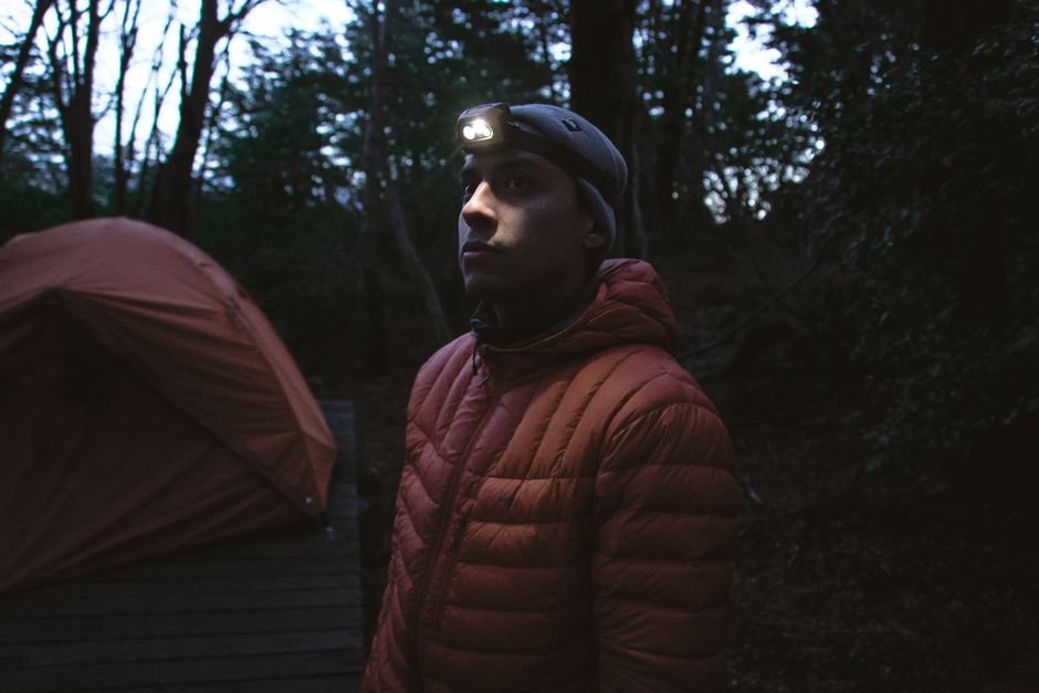 a man wearing a headlamp secured on his forehead at a forest campsite at night