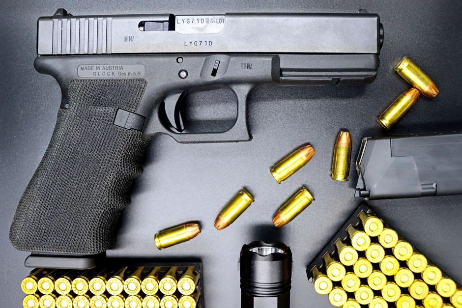 glock pistol with an attached tactical flashlight and ammunition on a dark surface