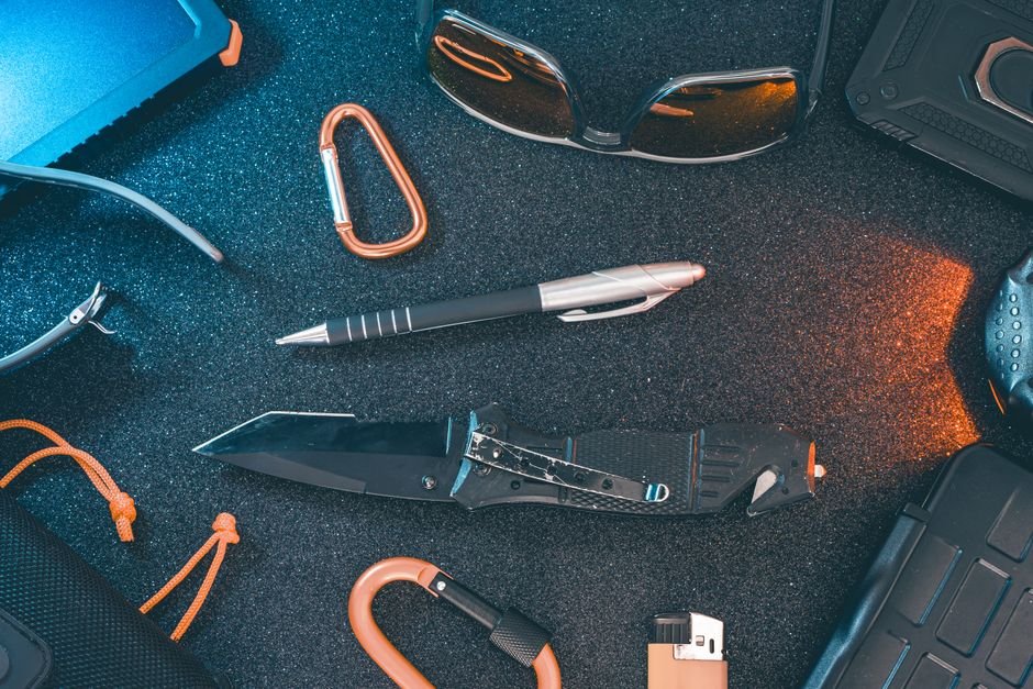 flat lay of everyday carry personal defense tools including knife and pen