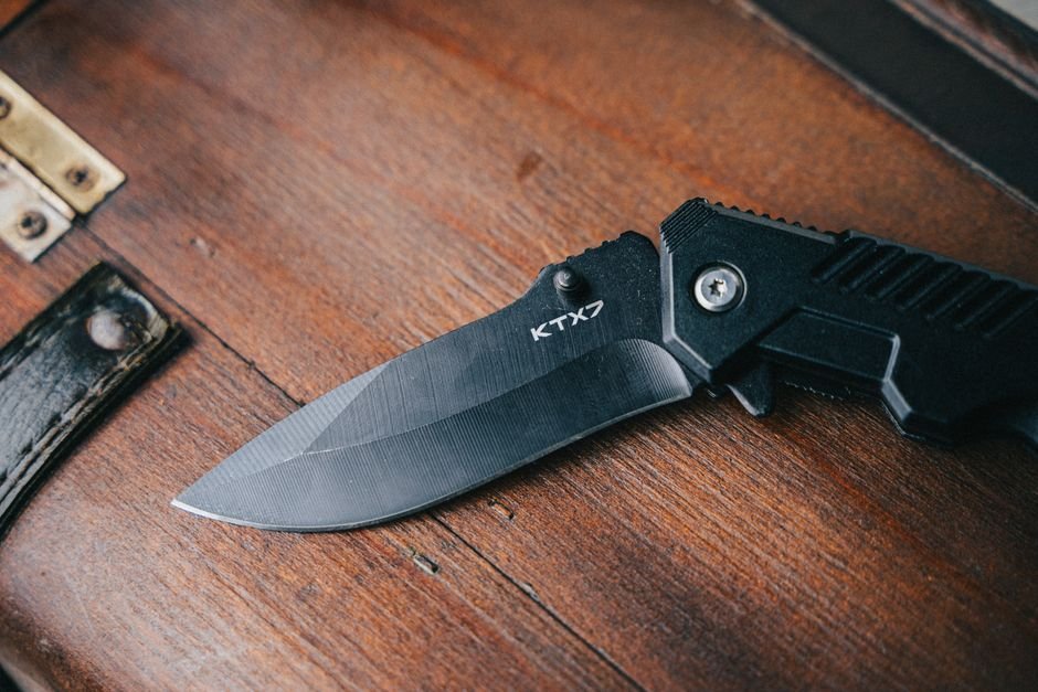 close up of a black folding knife on a textured wooden surface