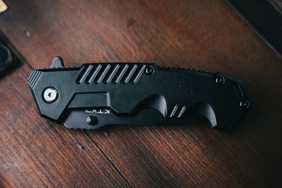 black folding edc pocket knife on wooden surface