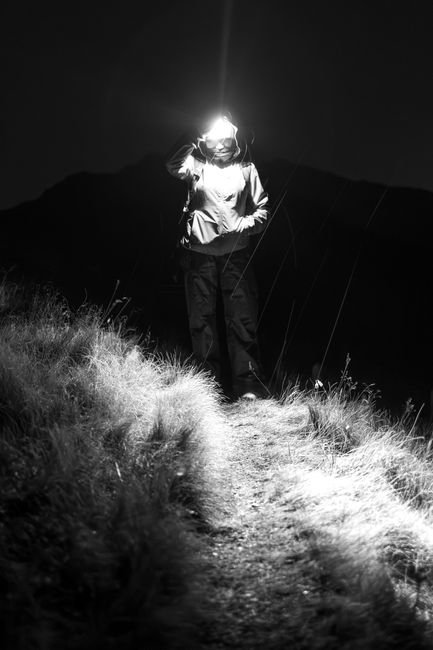 a hiker's headlamp beam cutting through a dark trail at night