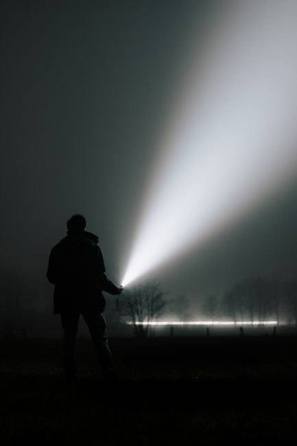 a flashlight beam cutting through dense fog at night showing how far the light reaches