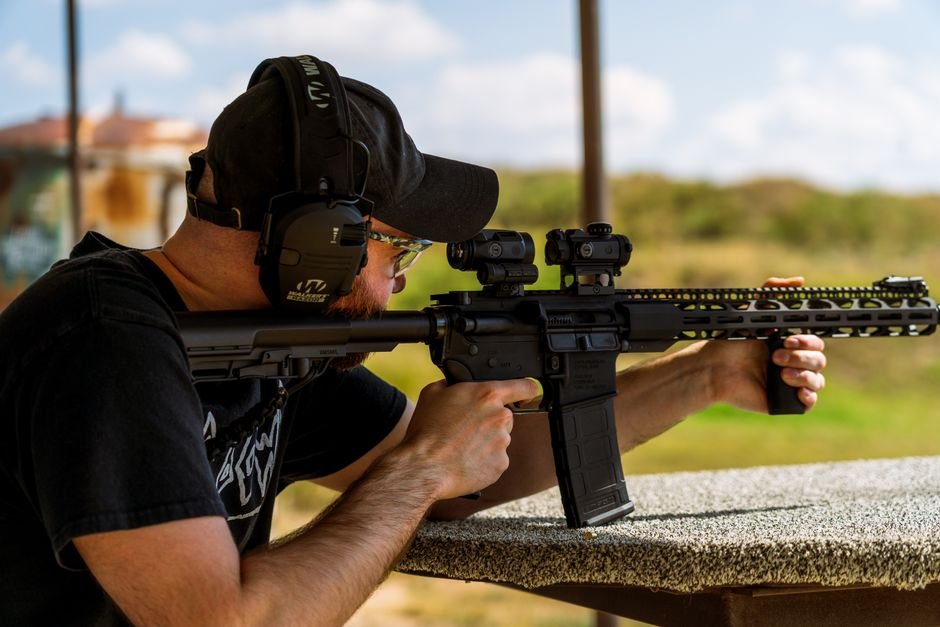 shooter aiming a rifle at an outdoor shooting range on a clear day