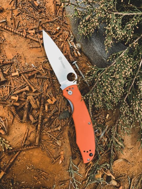 orange handled folding knife resting on a natural outdoor surface
