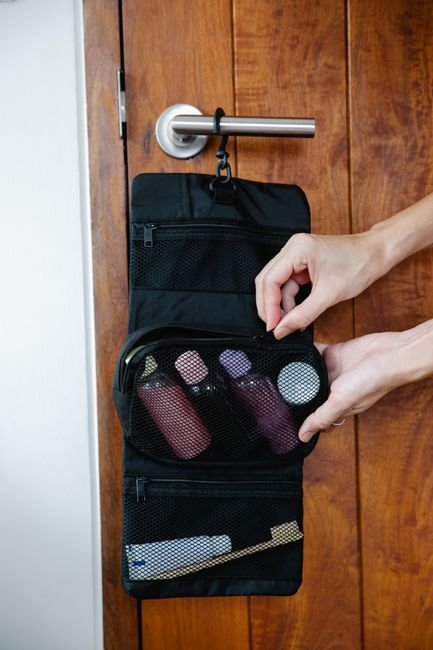 a person zipping a travel toiletry bag packed with cosmetic and grooming products