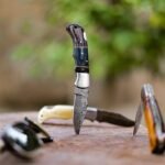 several knives with ornate handles stand upright in a weathered wooden surface outdoors with a blurred green background