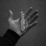 a hand holding an engraved folding pocket knife shown in monochrome