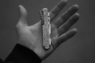 a hand holding an engraved folding pocket knife shown in monochrome