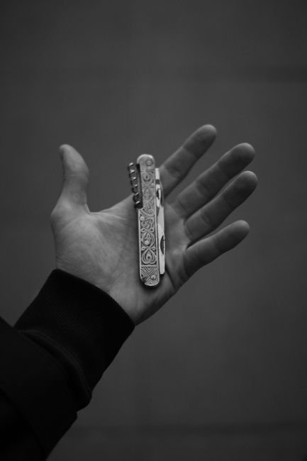 a hand holding an engraved folding pocket knife shown in monochrome