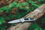 silver folding knife resting on a weathered tree branch in a forest setting