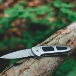 silver folding knife resting on a weathered tree branch in a forest setting