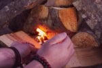 hands feeding tinder into a small fire being coaxed alight