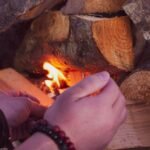 hands feeding tinder into a small fire being coaxed alight