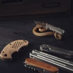 several multitools and a knife laid out on a dark wooden surface
