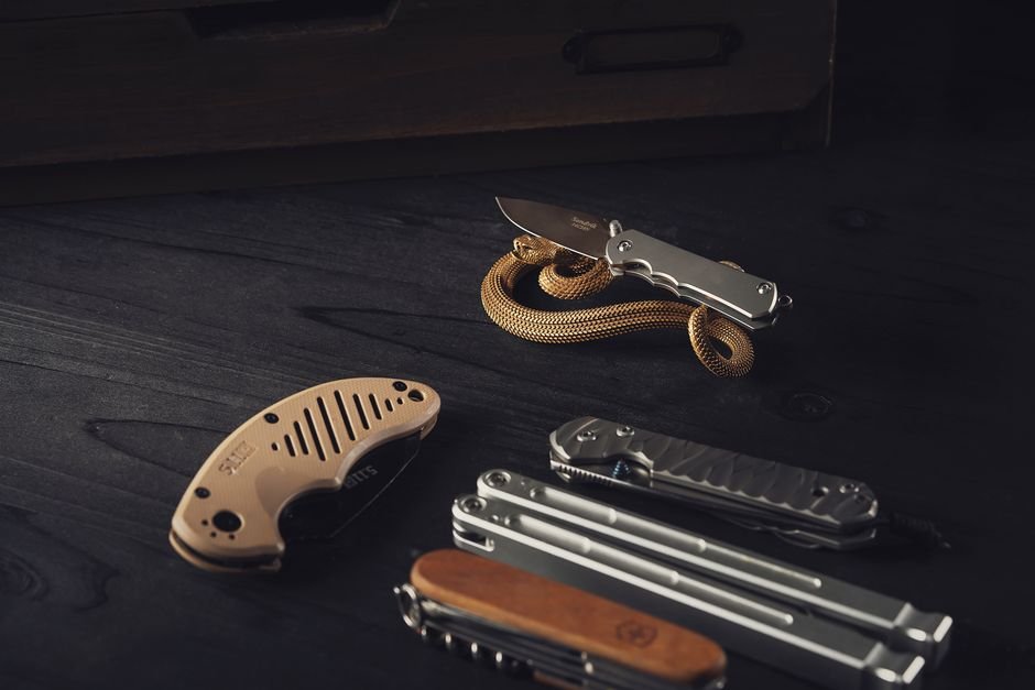 several multitools and a knife laid out on a dark wooden surface