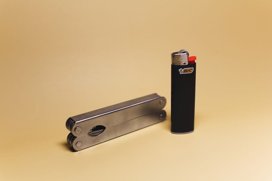 a metal multitool and a lighter arranged flat on a plain background