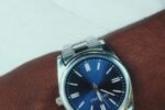 A silver wristwatch with a blue dial worn on the wrist