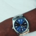 a silver wristwatch with a blue dial worn on the wrist